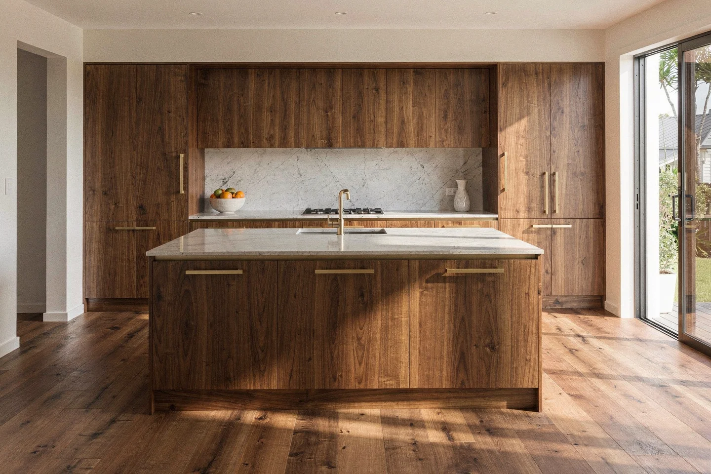 The same Sunshine Beach kitchen after Grainline: walnut island, honed stone and aged brass