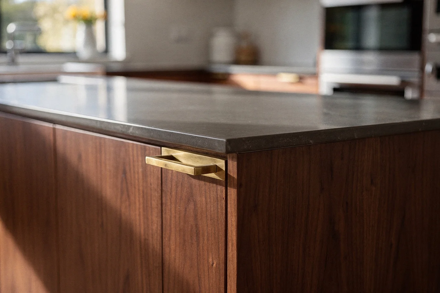 Honed stone island edge meeting bookmatched walnut with a let-flush aged-brass handle